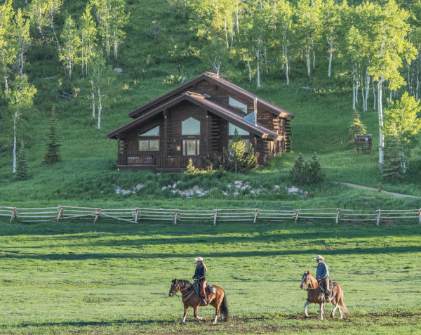 horses riding in front of a family cabin at a luxury ranch